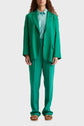 Person wearing a bright green suit with a light blue shirt and brown sandals, standing against a plain light background. The persons head is partially visible, and their hands rest by their sides.