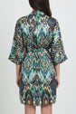 A person wearing a short, belted robe with a colorful, abstract pattern and ceinture amovible stands facing away, showing the back of the garment against a plain background.