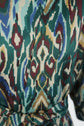 Close-up of fabric with a bold, multicolored Ikat print in teal, green, burgundy, beige, and blue tones, featuring an abstract, geometric motif ethnique and a ceinture amovible tied at the waist.
