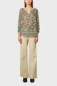 A person wearing a patterned, long-sleeve blouse with a split neckline and beige wide-leg pants, standing against a plain, light background.