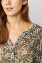 A woman with long brown hair wears a beige blouse with a blue and brown floral pattern and buttons. Only her lower face, neck, and shoulder are visible.