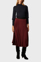 Woman wearing a navy long-sleeve sweater, a burgundy jupe midi plissée, and black knee-high boots, standing against a plain light gray background.