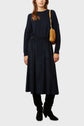 A woman wearing a navy velours côtelé sweater and matching jupe midi, black boots, and carrying a tan shoulder bag stands against a plain light background for a look casual-chic.