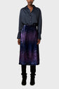A person wearing a dark blue button-up shirt, a shiny blue and purple sequin skirt, and black pants with black shoes, standing against a plain light grey background.