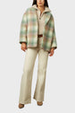 Woman wearing a pastel plaid manteau court en laine mélangée, beige zip-up sweater, cream high-waisted flared pants, and tan pointed-toe shoes, standing against a plain light background.