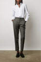 A person stands with hands in pockets, wearing a white button-up shirt, grey tailored pants, and black loafers against a plain background.