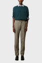 Person wearing a teal sweater over a striped shirt with rolled cuffs, beige trousers with a drawstring, and black shoes, standing against a plain light gray background.