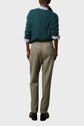 Person standing with back to camera, wearing a teal sweater over a striped shirt, beige trousers, and black shoes. The outfit looks casual and comfortable. The background is plain and light-colored.