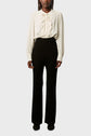 Person wearing a cream long-sleeve blouse with ruffles down the front, paired with a black pantalon large taille haute in laine mélangée, and black shoes, standing against a plain light background.