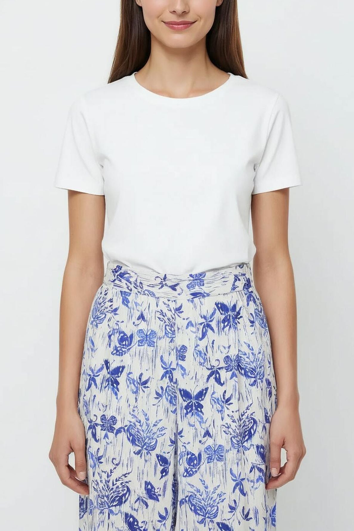 Woman wearing a plain white short-sleeve t-shirt and high-waisted, wide-leg cream pants with a blue imprimé fleuri, standing against a plain light background.