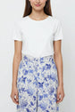 Woman wearing a plain white short-sleeve t-shirt and high-waisted, wide-leg cream pants with a blue imprimé fleuri, standing against a plain light background.