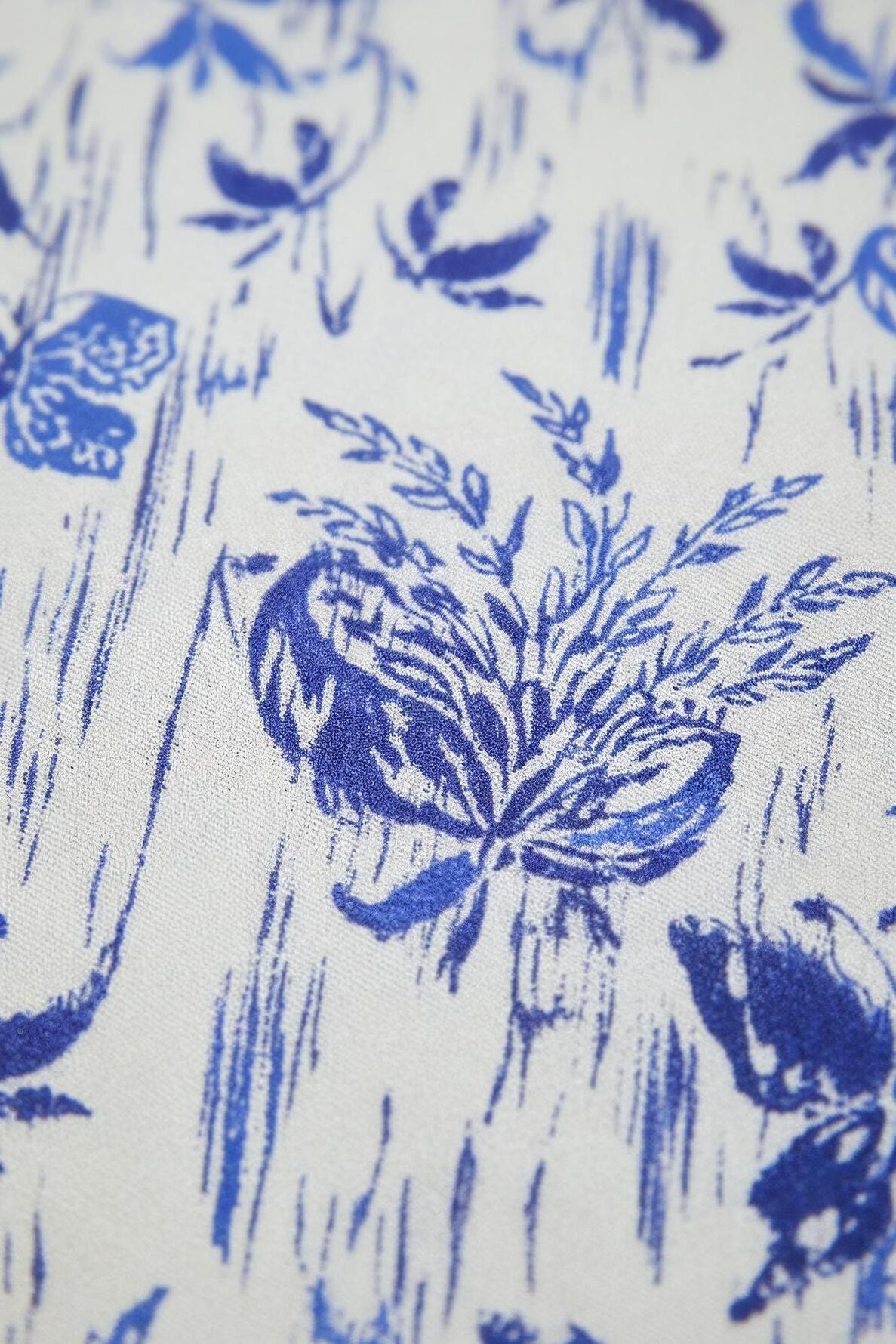 Close-up of a fabric with a blue imprimé fleuri on a white background, featuring leaves and abstract lines for a textured look—perfect for creating a pantalon large or taille haute design.