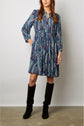 Woman wearing a knee-length, long-sleeve blue paisley dress with a cinched waist and black knee-high boots, standing against a plain light background.