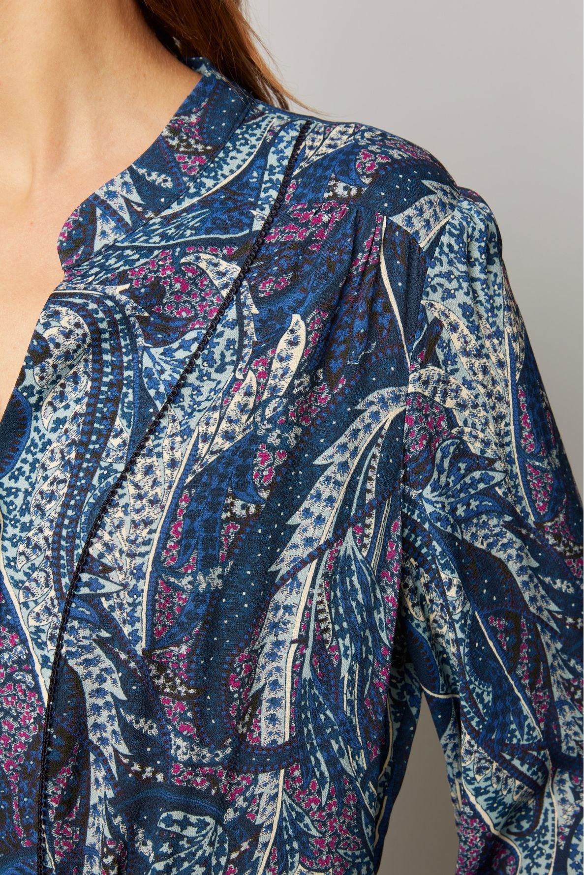 Close-up of a person wearing a blue patterned shirt with abstract leaf and dot designs in white, navy, and pink tones. The shirt has a collar and buttons; only part of the neck, shoulder, and upper chest are visible.