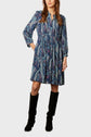 Woman wearing a long-sleeve, blue paisley-patterned dress with a gathered waist and black knee-high boots, standing against a plain light background.