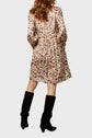 Woman wearing a cream floral-print dress with long sleeves and a gathered waist, paired with black knee-high boots, facing away from the camera against a plain background.