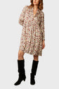 Woman wearing a loose, knee-length, long-sleeve floral dress with a v-neck, paired with tall black boots, standing against a plain light background.