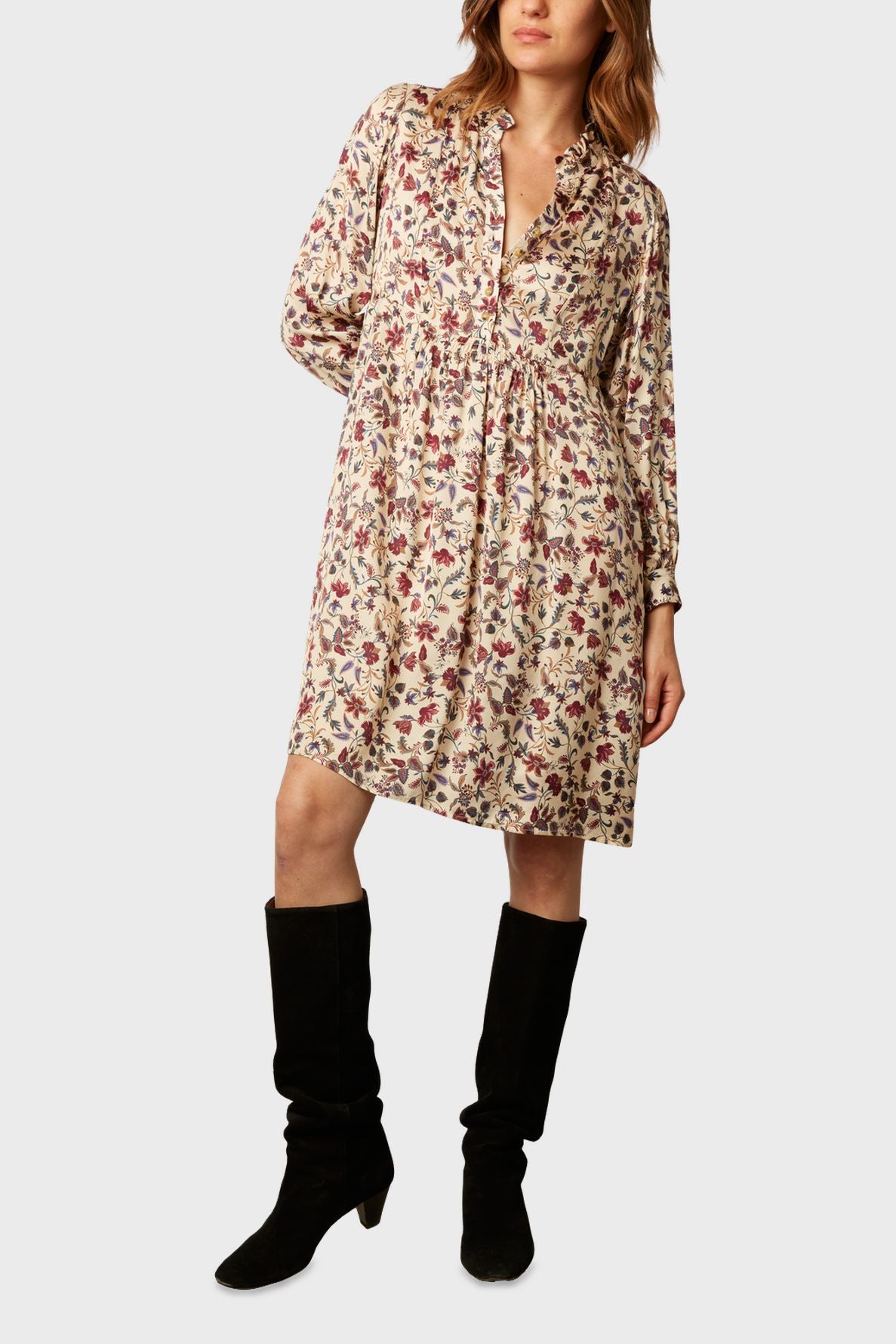Woman wearing a loose, long-sleeved, knee-length dress with a floral pattern in red and purple tones, paired with black knee-high boots.
