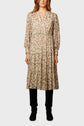 A woman wearing a long-sleeved, floral-print knee-length dress with a V-neckline, reminiscent of an imprimé cachemire style, paired with black pants and black shoes, standing against a plain light background.