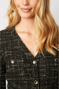 A woman with wavy blonde hair wears a textured black and white jacket with prominent buttons. The image is cropped at her nose and below the shoulders.