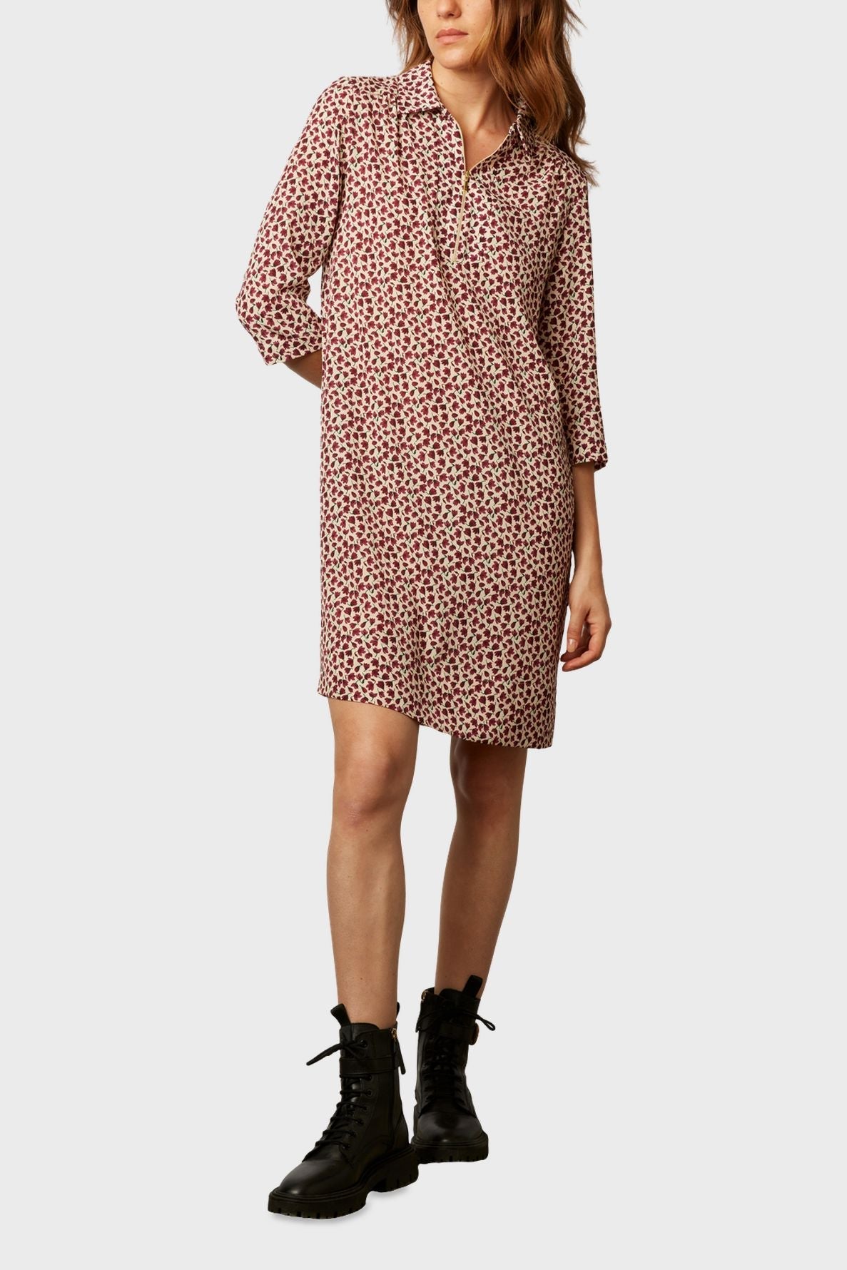 Woman wearing a knee-length, long-sleeved dress with a red and white floral pattern, paired with black lace-up combat boots, standing against a plain background.
