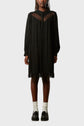 A person wearing a loose black long-sleeve dress with sheer panels at the chest and hem, reminiscent of the dentelle bohème chic style, paired with white socks and black loafers, standing against a plain light background.