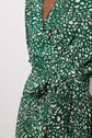 Close-up of a person wearing a green and white patterned wrap dress with a tied belt at the waist. The fabric features an abstract spotted design. Only part of the torso and dress are visible.