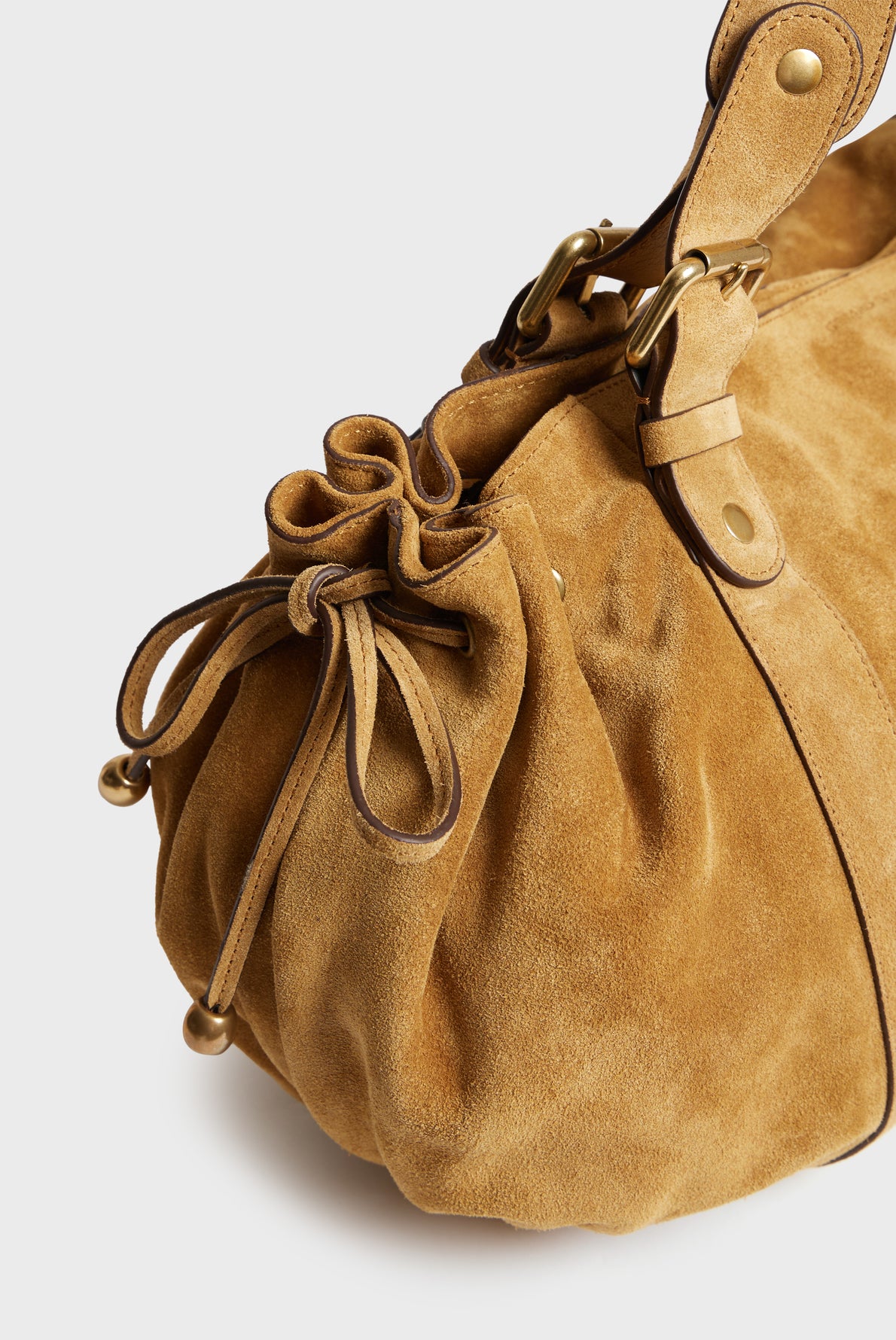 Close-up of a tan cuir velours sac à main Darel with brass hardware, a drawstring closure, and a rounded, gathered shape. The handle attaches with straps and rivets.