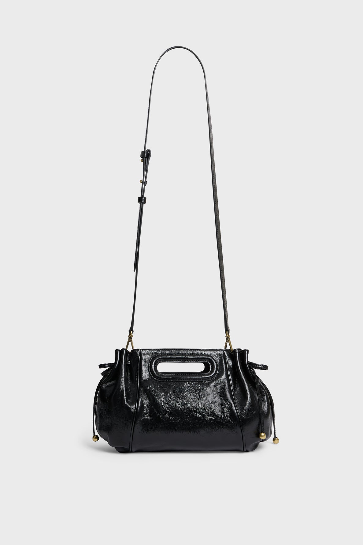 A shiny black cuir froissé leather sac à main with a long adjustable shoulder strap, cut-out handle, gathered sides, and gold hardware, displayed against a plain light gray background.