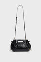 A shiny black cuir froissé leather sac à main with a long adjustable shoulder strap, cut-out handle, gathered sides, and gold hardware, displayed against a plain light gray background.