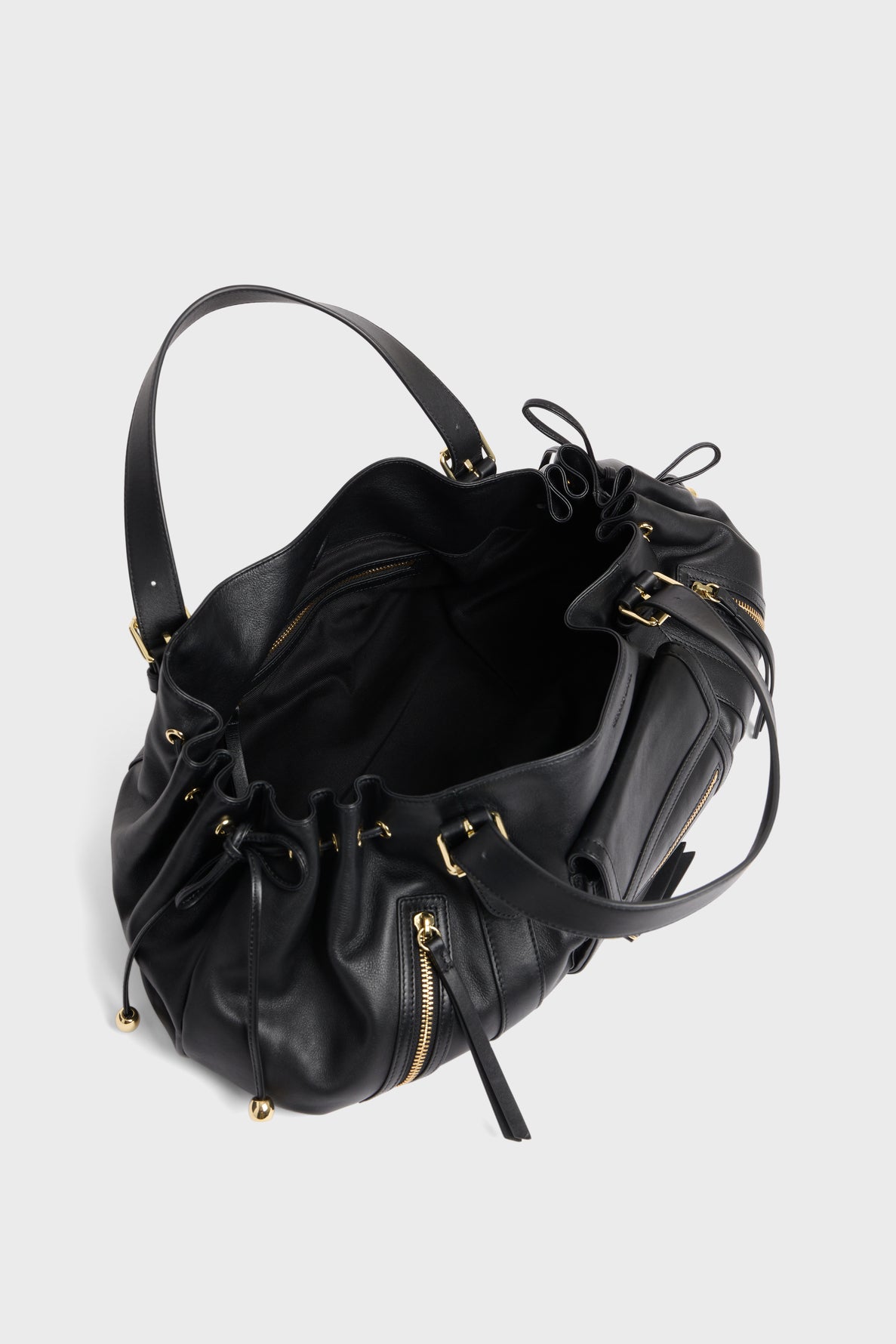 A black sac à main en cuir délicat with gold hardware, drawstring closure, side poches zippées, and an open interior is shown on a plain light gray background.