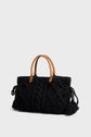 A black sac à main en tricot with braided patterns, featuring tan leather handles and decorative tassels on the sides, showcases the charm of laine souple artisanale craftsmanship. This Maison Darel handbag is set against a plain light gray background.