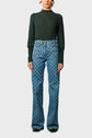 A person wears a dark green long-sleeve ribbed top and high-waisted blue jeans with a repeating pattern. The jeans have front pockets and flared legs. Only the persons torso and legs are visible.