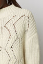 A close-up of a cream-colored pull col montant knit sweater with a textured, patterned design in laine mélangée, worn by a person with dark skin and braided hair.