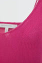Close-up of a bright pink knit fabric, possibly a débardeur femme or sweater, showing a small area of visible wear or thinning near the shoulder seam. A white clothing tag is partially visible in the background.