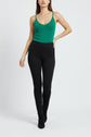 A woman stands against a white background wearing a green top sans manche, high-waisted black pants, and black shoes.
