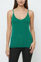 Woman wearing a sleeveless green top sans manche with spaghetti straps and black pants, standing against a plain white background.