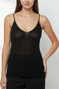 A woman wearing a débardeur femme—a black, thin-strapped, semi-sheer camisole—and black pants stands against a plain light background.