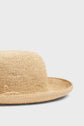 A close-up of a woven raphia chapeau femme with a wide brim, shown against a plain light gray background. Only the lower half of this elegant chapeau été is visible in the image.
