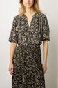 Woman wearing a black and beige floral patterned crêpe georgette dress with short sleeves and a v-neck, standing against a plain light background.