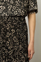 A person wearing a black crêpe georgette dress with a beige motif floral pattern stands against a plain background. Only the side of the torso, arm, and hand are visible.