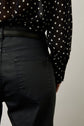 A person wearing high-waisted black jeans and a black, long-sleeved, polka dot blouse is shown from the waist down, with the focus on their back pocket and blouse detail.