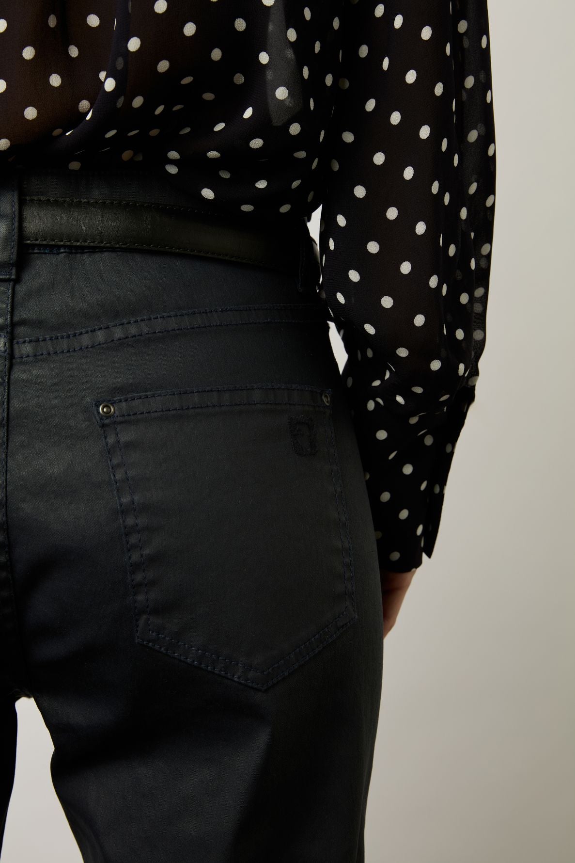 A person wearing black high-waisted jeans and a black blouse with white polka dots, shown from the back and slightly to the side.
