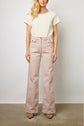 Woman standing against a plain background, wearing a cream short-sleeve textured top, light pink wide-leg pants with front pockets, and beige shoes. Her face is partially out of the frame.