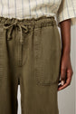 A person wears olive green drawstring pants with large front pockets and a cream textured top with blue stripes. Only the torso and one hand are visible.