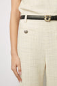 A person wearing cream-colored textured pants and a matching top with a black belt featuring a gold buckle. Only the lower torso and left arm are visible.