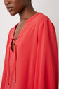 A person wearing a red blouse with a v-neckline and crisscross tie detail—reminiscent of a robe courte fluide—shown from the shoulders up and facing left.