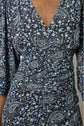 Close-up of a person wearing a dark blue dress with a V-neckline and floral paisley pattern in light blue, white, and teal colors. The fabric is ruched at the waist and the sleeves are three-quarter length.