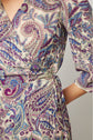 Close-up of a person wearing a bohème-chic robe portefeuille with long sleeves, featuring a vibrant imprimé cachemire in purple, blue, and cream tones. Only part of the upper body and one arm are visible.