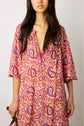 A woman wearing a loose-fitting robe longue fluide with a pink and purple paisley imprimé ethnique and a deep V-neckline, standing against a plain background—an effortless look from the latest collection Studio.